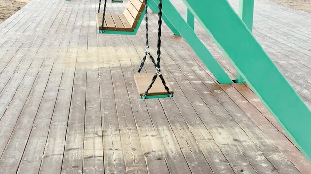 POV walkthrough of an empty wooden playground structure in Pushkin, Russia, shot on stabilizer in slow motion. Empty swings sway gently over the boardwalk, evoking a peaceful nostalgic feeling.