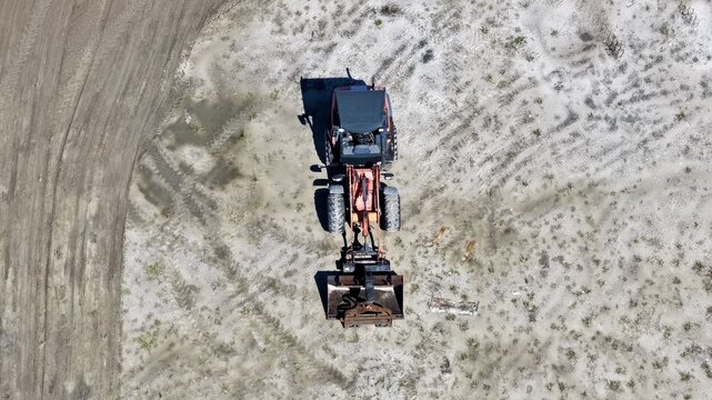 Aerial view of a tractor parked on a dirt construction site showing tire tracks in the sand and clear ground details in World Golf Village, Florida, United States.