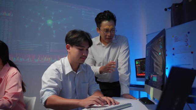 Asian data analysts collaborating on a project and analyzing cryptocurrency stock market charts on a computer at night