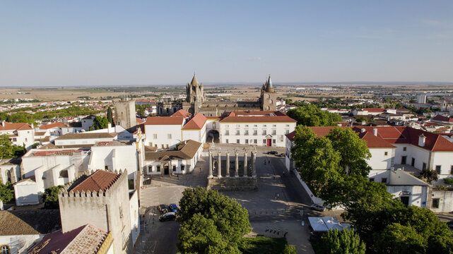 Aerial view of the Roman Temple of Evora surrounded by historic white buildings, red-tiled rooftops, and the Evora Cathedral in the background in Evora, Distrito de Evora, Portugal.
