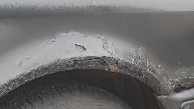 Close up of a corroded car fender with severe rust damage. Bubbling paint and decay revealing oxidized metal on an old vehicle body