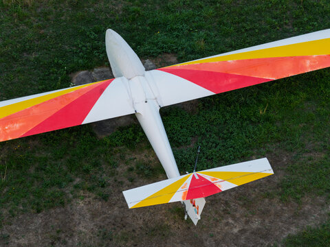 Aerial view of a glider with white, red, and yellow wings flying over a green grassy field in the United Kingdom.
