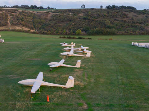 Aerial view of several gliders parked in a row on a grassy airfield with rolling hills in the background in the United Kingdom.