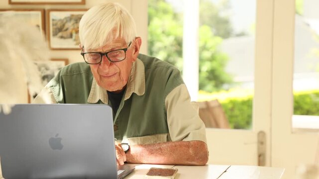 elderly man (90) looking at laptop computer in light filled room