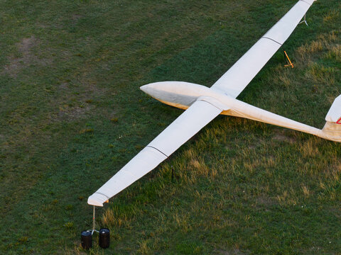 Aerial view of a white glider parked on a grassy field with a support stand under its wing tip in the United Kingdom.