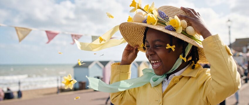 A laughing little girl wearing a festive handmade Easter hat walking happily outdoors by the sea