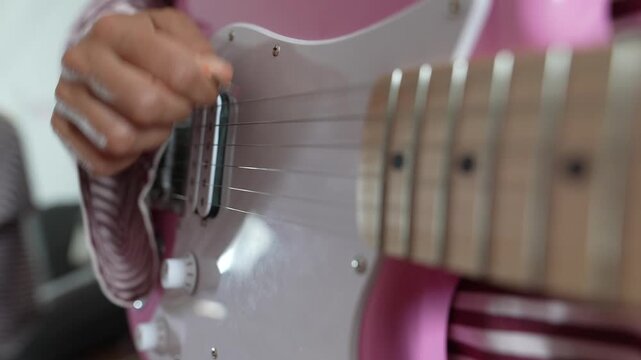 Close-up of fingers plucking the strings of a pink electric guitar