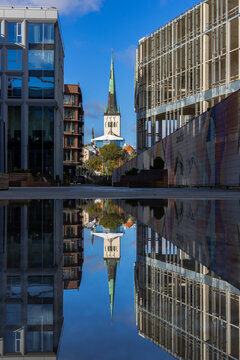 The spire of St Olaf's Church and the modern buildings along the street are mirrored in a still puddle in Tallinn, Estonia. 