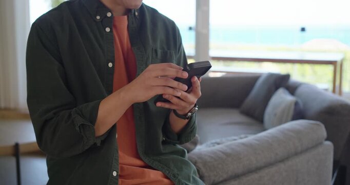Seated man is cradling phone, initiating taps and swipes on couch near balcony checking messages