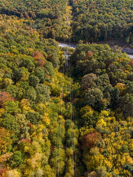 Aerial view of a power line corridor cutting through a dense autumn forest with vibrant fall foliage in Feleacu, Cluj County, Romania.