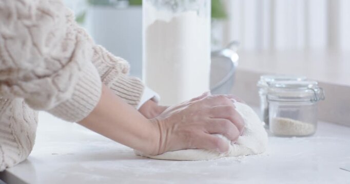 Prompted by floured dough mound, baker's hands are folding and shaping loaf for proofing on counter