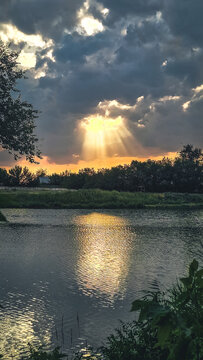 Golden sun rays breaking through dark storm clouds over lake at sunset