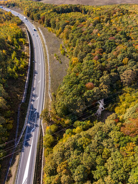 Aerial view of a highway winding through a dense forest with vibrant autumn foliage and power lines crossing the landscape in Feleacu, Cluj County, Romania.