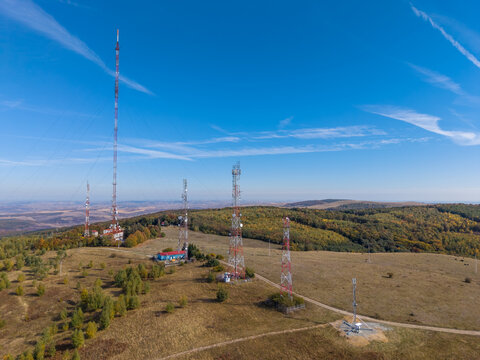 Aerial view of the Feleacu 311A Cluj telecommunication towers standing on a grassy hill surrounded by autumn forests in Cluj-Napoca, Judetul Cluj, Romania.