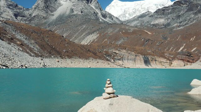 Breathtaking mountain landscape featuring traditional stone cairn standing on rock by tranquil turquoise lake, with majestic snow peaks of himalayas towering in background
