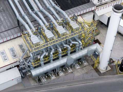 Aerial view of an industrial facility featuring complex pipe systems, ventilation units, and a tall chimney stack on a factory rooftop in Lesser Poland Voivode, Poland.