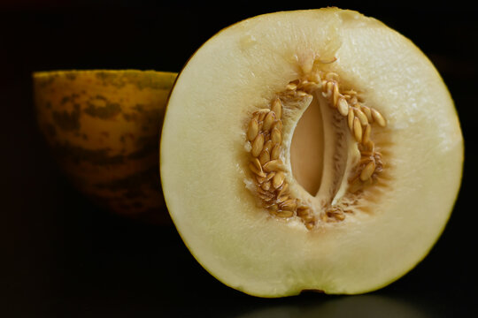 Two half yellow melon on black background. Sweet organic melon cut of half with seeds. Food and fruit background, Health , vitamins concept.