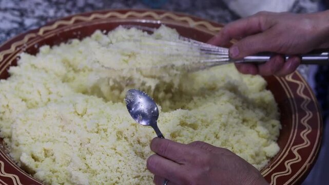 Hand fluffing Moroccan couscous with spoon and whisk in clay plate