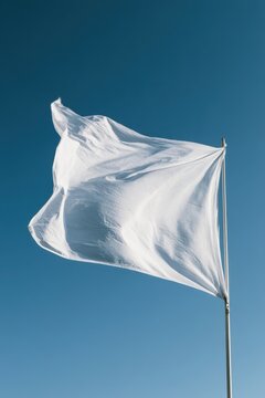 Close-up of a crisp white flag fluttering on a slim flagpole against a clear blue sky