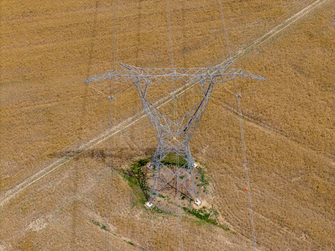 Aerial view of a large metal electricity pylon standing in a dry, golden agricultural field in Riebeek-Kasteel, Western Cape, South Africa.