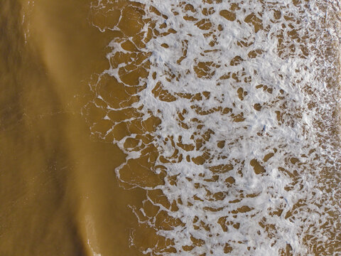 Aerial view of white sea foam washing over the sandy beach at the shoreline in Talacre, Flintshire, United Kingdom.