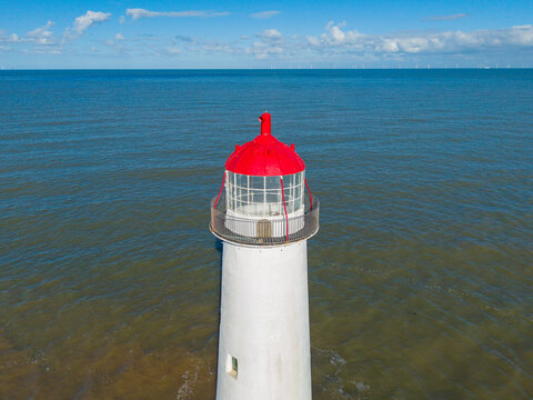 Aerial view of Point of Ayr Lighthouse with its distinctive red top, surrounded by the calm waters of the Irish Sea under a clear blue sky, Talacre, Flintshire, United Kingdom.