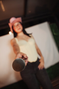 Beautiful woman wearing a cowboy hat and holding a microphone, singing at a karaoke session.