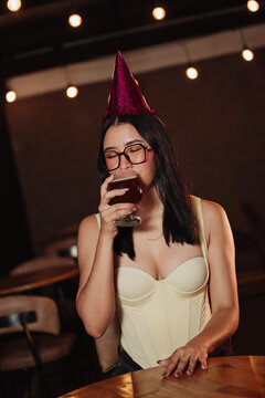 beautiful woman wearing a birthday hat, holding a beer in a bar