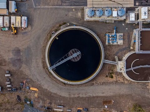 Aerial view of a circular wastewater treatment clarifier with industrial tanks and infrastructure in The Common, Queensland, Australia.