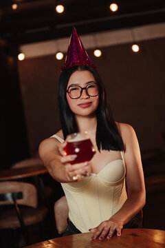 beautiful woman wearing a birthday hat, holding a beer in a bar