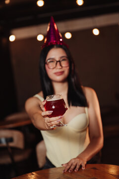 beautiful woman wearing a birthday hat, holding a beer in a bar