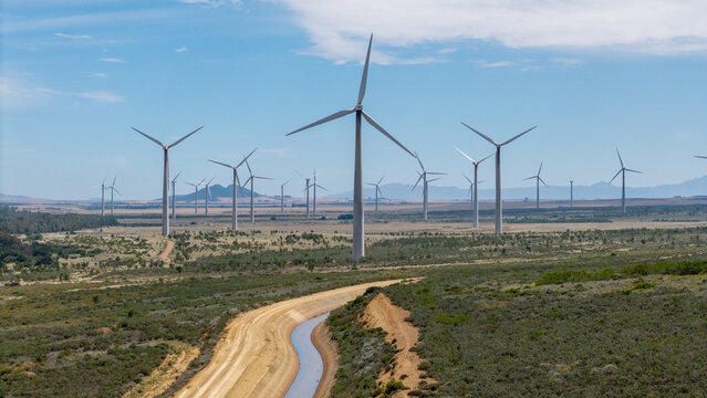 Aerial view of wind turbines in a rural landscape with a canal in the foreground near Hermon, Western Cape, South Africa.