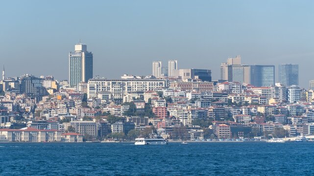 Taksim skyline in Istanbul, Turkey, seen from the Bosphorus, with dense hillside neighborhoods and a white passenger boat crossing the water