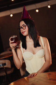 Beautiful woman wearing a birthday hat holding a beer in a karaoke bar.