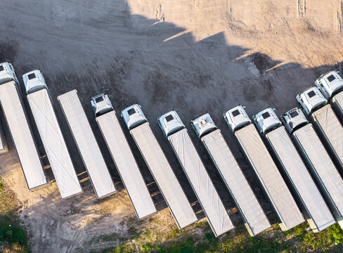Aerial view of a row of white semi-trucks parked in a dirt lot in Kwidzyn, Pomeranian Voivodeship, Poland.