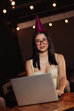 Beautiful woman wearing a birthday hat, using her laptop in a bar. Concept: working on one's birthday.