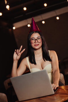 Beautiful woman wearing a birthday hat, using her laptop in a bar. Concept: working on one's birthday.