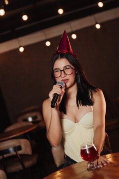 Beautiful woman wearing a birthday hat holding a microphone in a karaoke bar.
