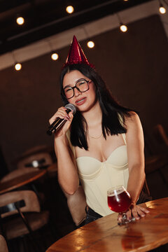 Beautiful woman wearing a birthday hat holding a microphone in a karaoke bar.