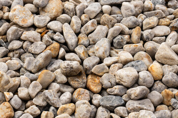 Natural rounded stones with varied gray, beige, and brown colors covering the frame in a detailed textured surface pattern and earthy stone background © Yahor