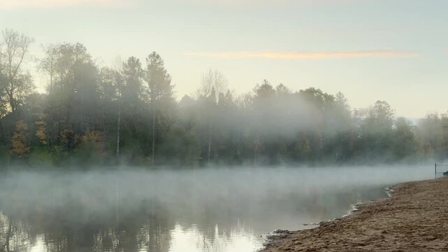 Thick fog rises over a calm park lake surrounded by trees during early dawn. A pan shot captures the tranquil water and misty shores, evoking a peaceful mood in Pushkin, slow motion.