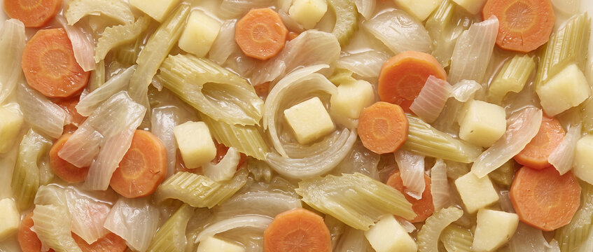 Mixed vegetable soup ingredients simmering in broth closeup top view