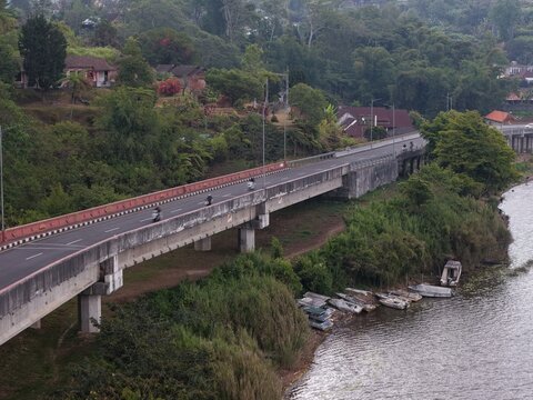 Aerial view of a concrete bridge spanning over the edge of Danau Beratan with small boats moored along the lush green shoreline in Baturiti, Bali, Indonesia.