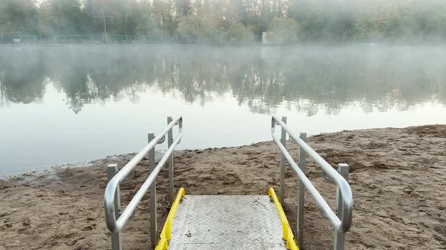 A tilt shot reveals a metallic lake ramp in Pushkin in slow motion. Morning mist rises over the calm water, creating a quiet, melancholic mood.