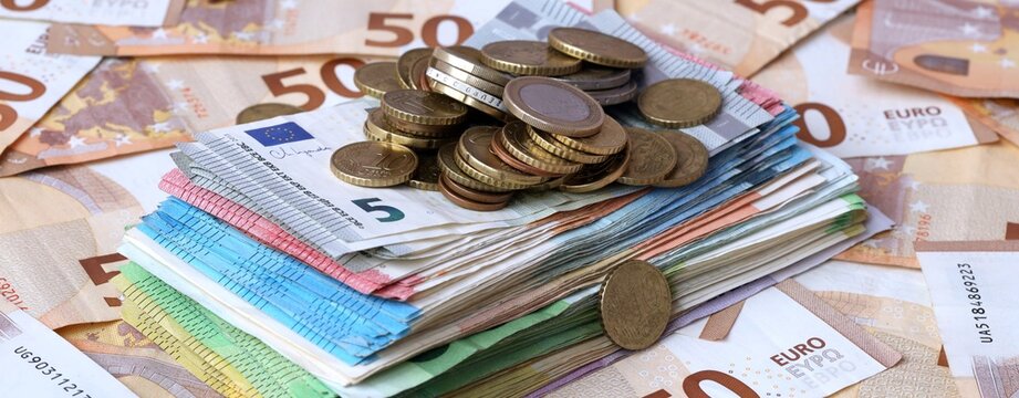 Pile of euro coins on stack of euro banknotes with fifty euro background