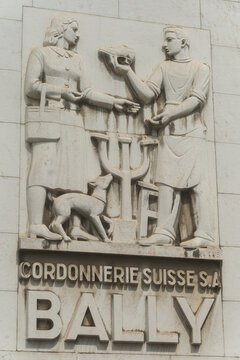 Antwerp, Belgium, july 08, 2026 : A carved Antwerp, Belgium,  stone relief showing two figures in a simple exchange and sign Bally a Swiss shoemaker, set into a weathered facade.