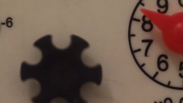 Close-up of a mechanical water meter with a rotating red needle and flow indicator wheel. Detailed footage of an operating domestic utility resource metering device