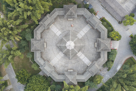 Aerial view of an octagonal traditional Chinese pavilion with grey tiled roofs surrounded by lush green trees and stone paved courtyards in Guilin, Guangxi, China.