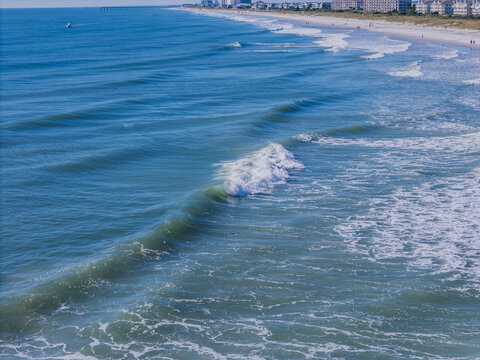 Aerial view of Atlantic Ocean waves rolling onto the sandy shore of Wrightsville Beach, with coastal buildings and a pier in the distance, Wrightsville Beach, North Carolina, United States.