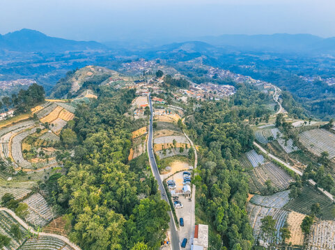 Aerial view of Linggarjati 2 surrounded by lush terraced agricultural fields, dense forests, and a winding road in the mountainous landscape of Kecamatan Kaliangkrik, Jawa Tengah, Indonesia.